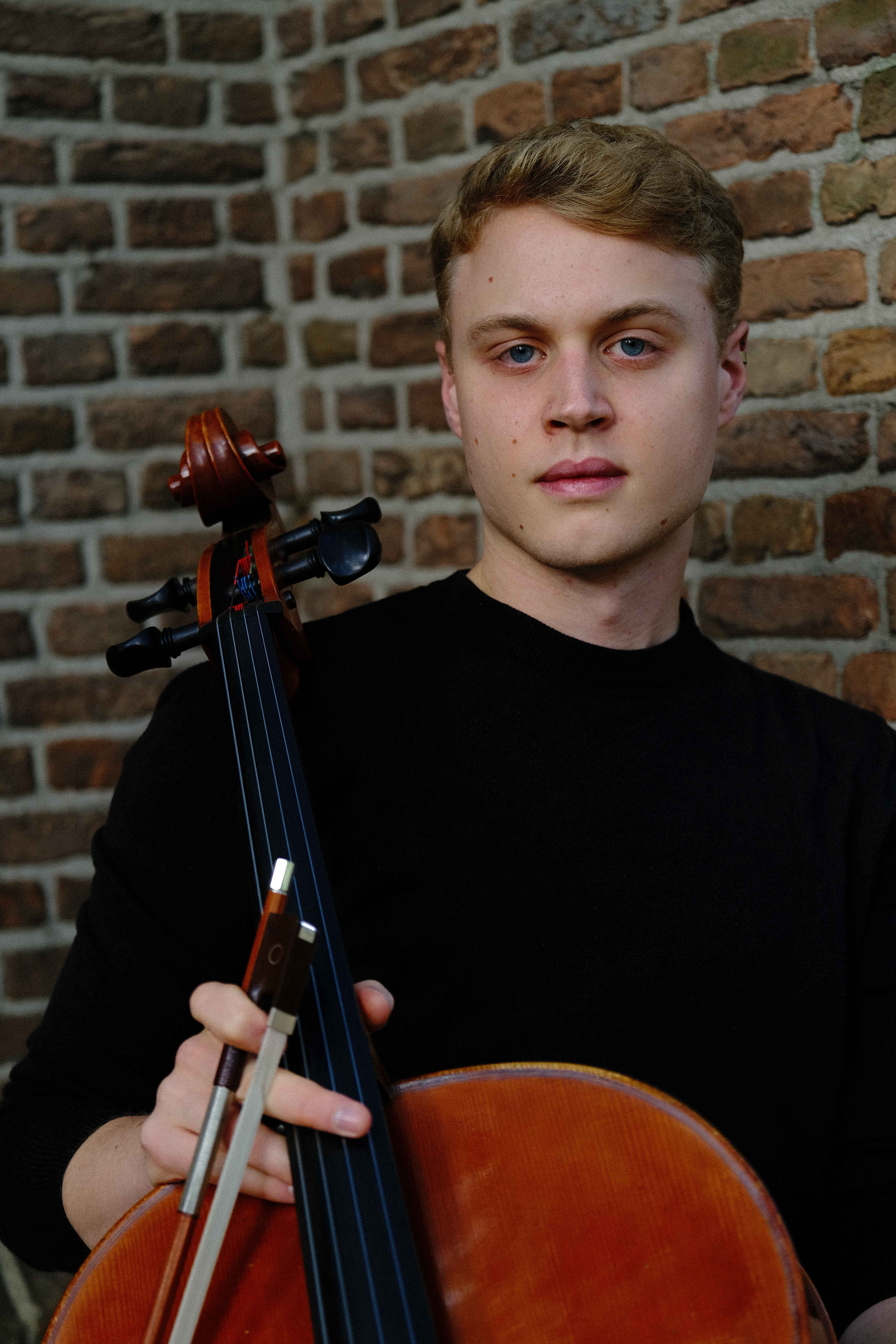 Luka Stefanović full-body with cello against historic architecture, The Hague 2023